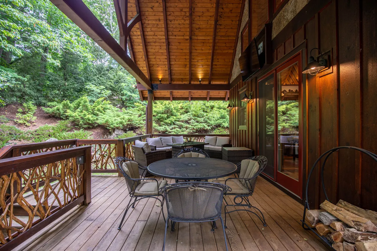 A spacious, circular outdoor dining table is set on a wooden deck, surrounded by comfortable seating and enclosed by a rustic wooden railing. Lush greenery fills the background, creating a serene and private setting ideal for al fresco meals, morning coffee, or evening stargazing.