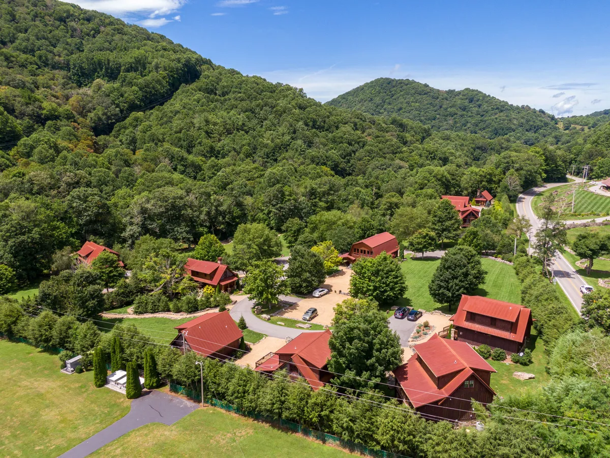 This exterior shot captures a cluster of red-roofed cabins nestled among lush greenery, with a winding driveway leading through the landscape and a scenic mountain backdrop. The view hints at a tranquil retreat where nature and community meet, offering a sense of the seasonal beauty described in the section.
