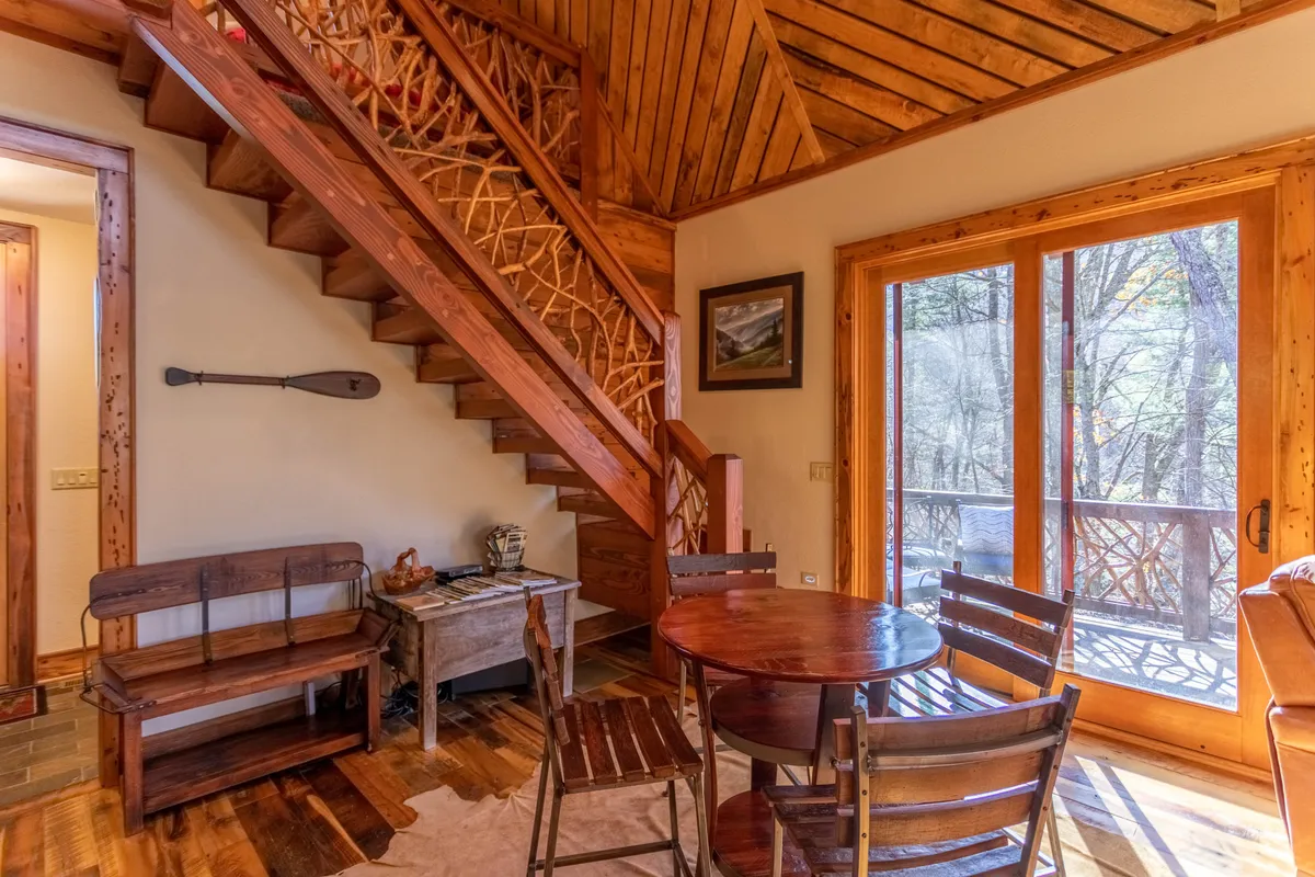 This interior shot centers on a wooden staircase adjacent to a dining table set beside large windows. The abundant natural light and surrounding woodwork create a warm and intimate atmosphere, perfect for family meals or game nights while admiring the landscape.