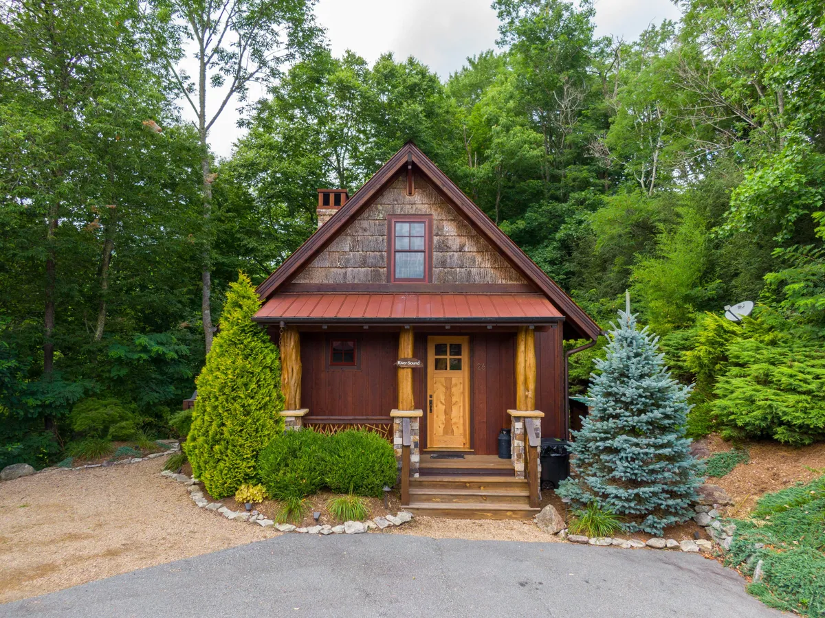 This image shows the inviting front entrance of River Sound Cabin, with wooden steps leading to the front door, surrounded by lush greenery and the cabin’s unique roof design. The natural landscape frames the cabin, hinting at the serene mountain setting and easy access to nature trails and downtown Banner Elk.