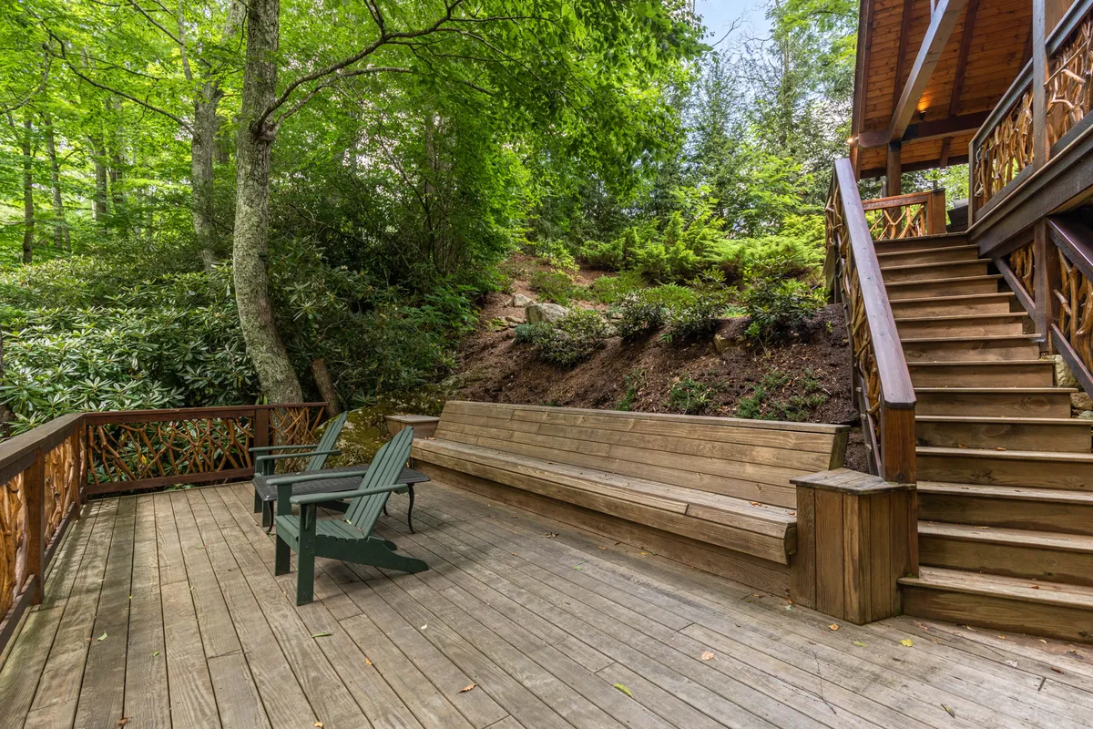 An inviting exterior shot of a wooden deck nestled among green trees, with benches and a staircase, evoking a sense of relaxation and togetherness. The setting is ideal for hosting barbecues, unwinding with nature, or enjoying sunsets with family and friends.