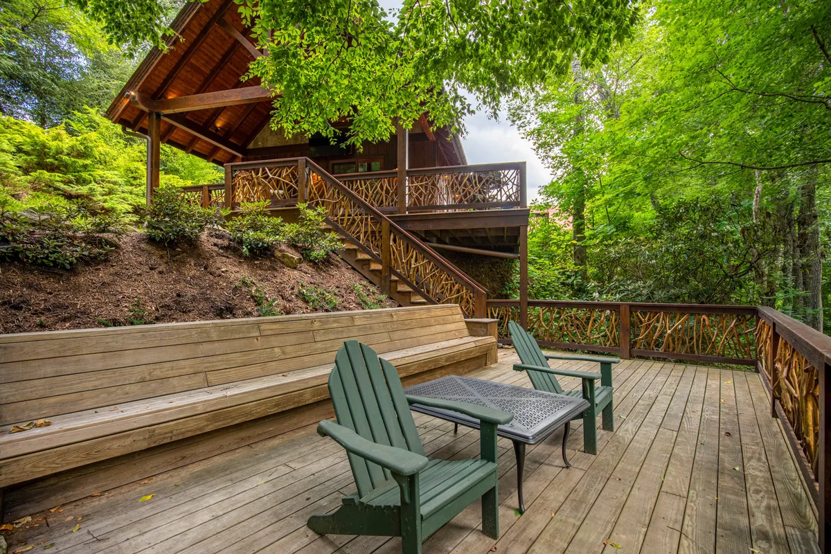 A tranquil wooden deck set amidst lush greenery, featuring green chairs and a cozy outdoor seating arrangement. The deck is surrounded by trees, inviting guests to relax and enjoy the serene riverfront environment.