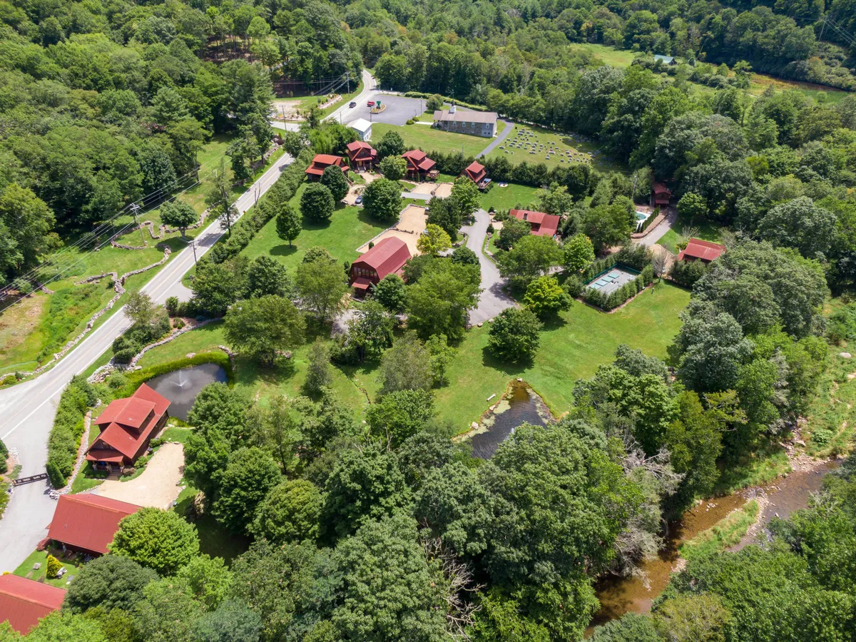 This image captures several red-roofed cabins set around a serene pond, with vibrant greenery and a country road weaving through the landscape. It evokes opportunities for hiking, fishing, and venturing into the local scenic towns, highlighting the sense of community and outdoor adventure.