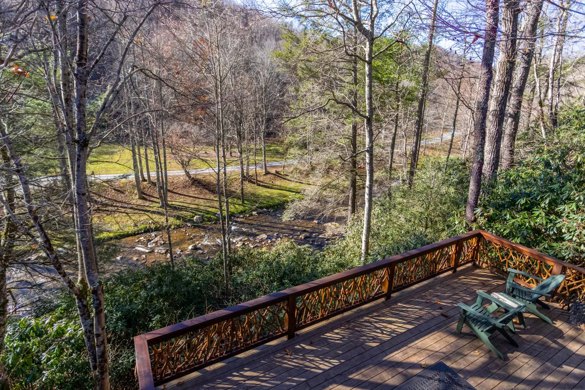 A tranquil deck with simple chairs provides intimate seating directly beside a stream, framed by mature trees. The natural setting and proximity to the water invite quiet contemplation, wildlife watching, and stargazing.