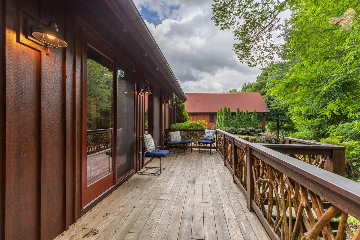 A wooden deck overlooks a sweeping landscape, featuring a cozy sitting area with chairs positioned to enjoy the views. The deck is surrounded by lush greenery, offering a peaceful and immersive outdoor experience.